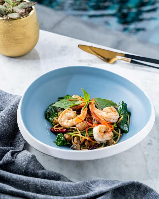 A shrimp and greens dish plated beside the swimming pool.