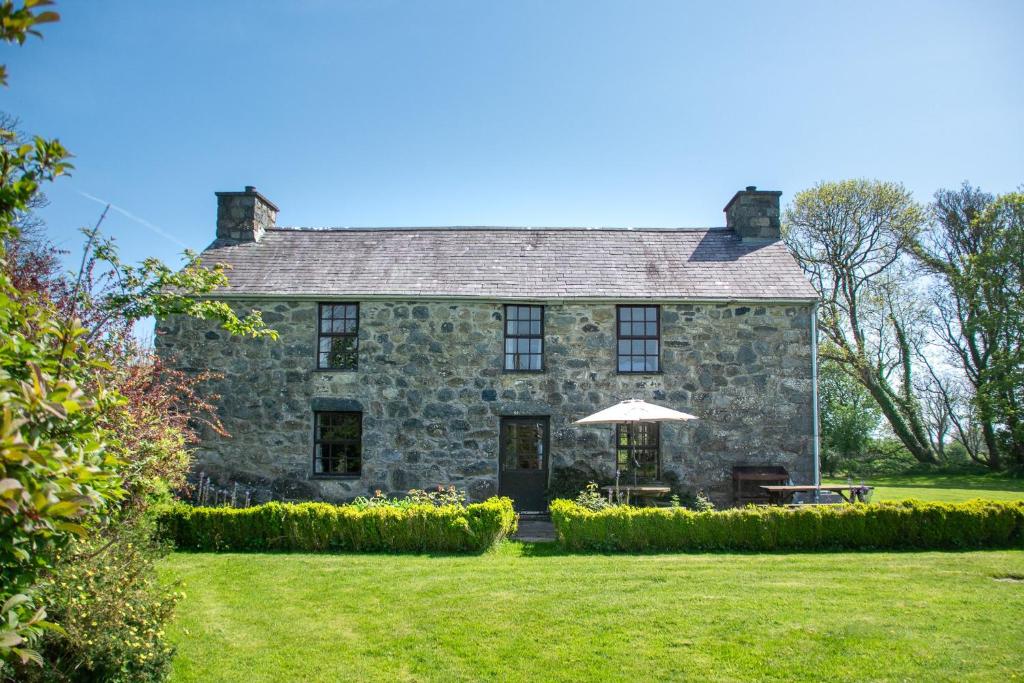 an old stone house with an umbrella in the yard at Glasfryn Fawr in Pwllheli