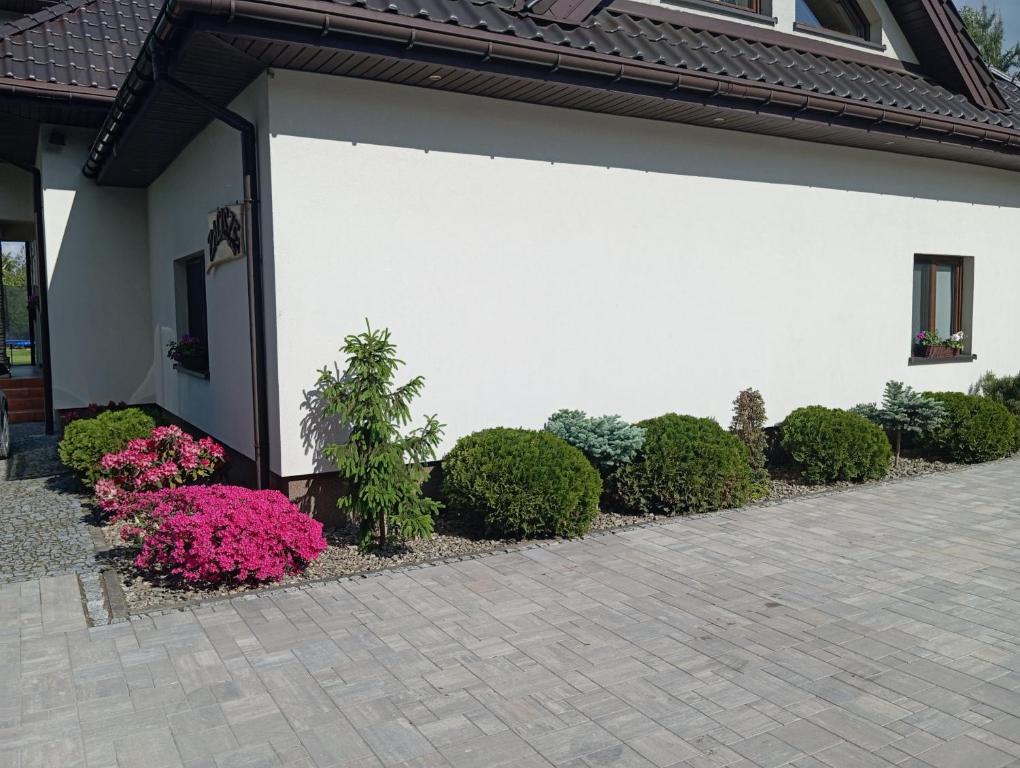 a white wall with some bushes and pink flowers at Zacisze in Rozalin