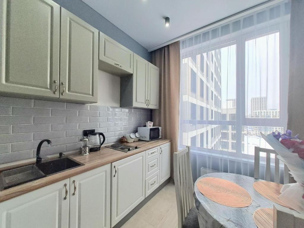 a kitchen with white cabinets and a sink and a window at Respublika LUX Уютная 2-комнатная квартира in Astana