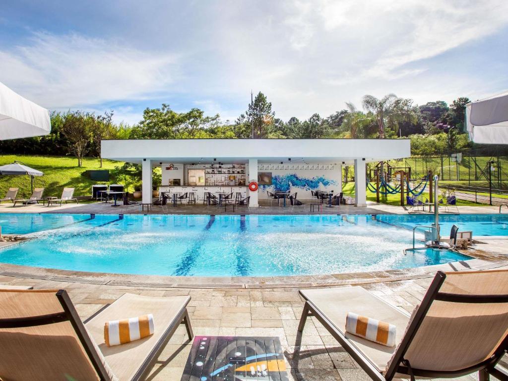 a pool at a resort with chairs and tables at Pullman Sao Paulo Guarulhos Airport in Guarulhos