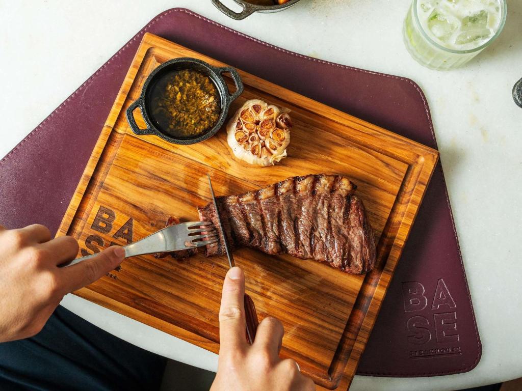 a person cutting a piece of steak on a cutting board at Pullman Sao Paulo Guarulhos Airport in Guarulhos