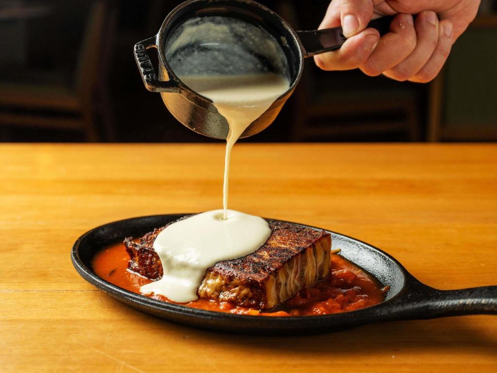 a person drizzling sauce on a plate of food at Pullman Sao Paulo Guarulhos Airport in Guarulhos