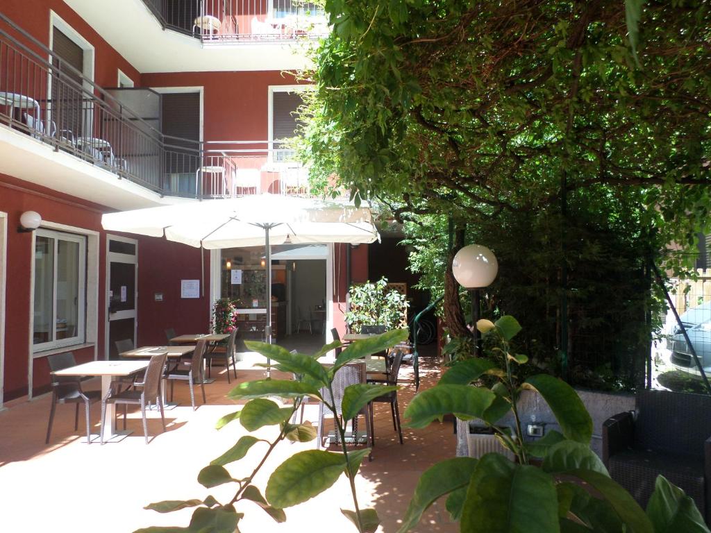 eine Terrasse mit Tischen, Stühlen und Sonnenschirmen in der Unterkunft Hotel Garnì Capinera in Garda