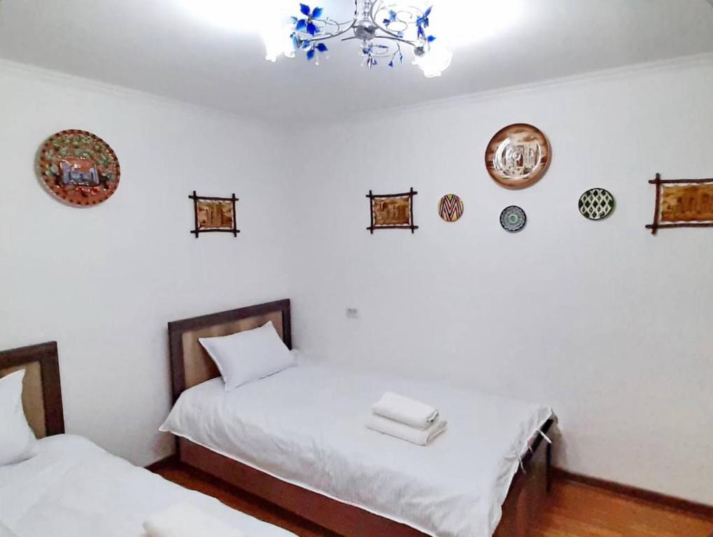 two beds in a room with white walls and a chandelier at Guesthouse Anora 1, Three minutes walk from Registan Square, The very Center of Samarkand in Samarkand