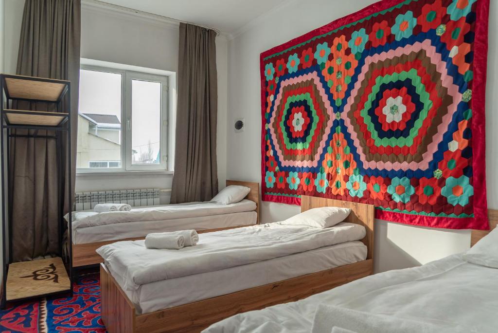 a room with three beds and a large painting on the wall at Baytor Guest House in Karakol