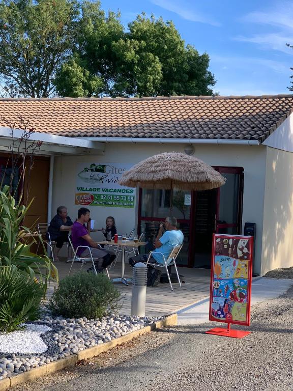 un groupe de personnes assises à une table à l'extérieur d'un restaurant dans l'établissement Village Vacances Les Rivières, à Maché