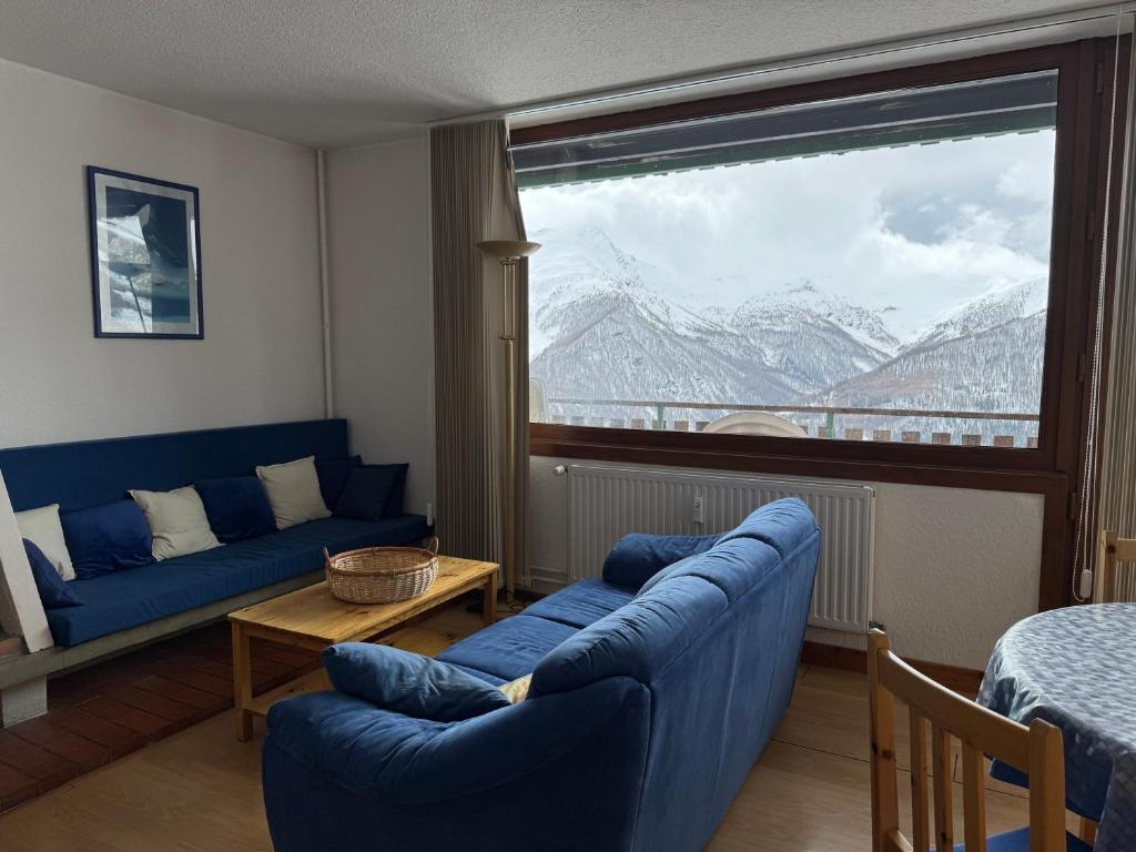 un salon avec un canapé bleu et une grande fenêtre dans l'établissement La Muande Appartement famille, à Orcières