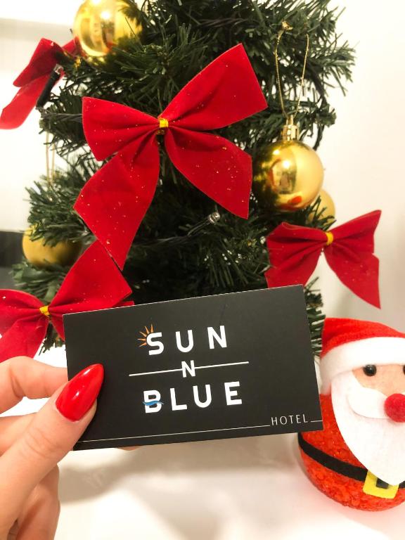 a person holding a sign in front of a christmas tree at Sun N Blue Hotel in Sarandë