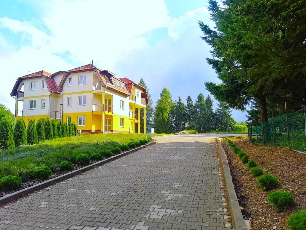 a yellow house on a road next to a tree at Levendula2 Apartman Bükkszentkereszt in Bükkszentkereszt