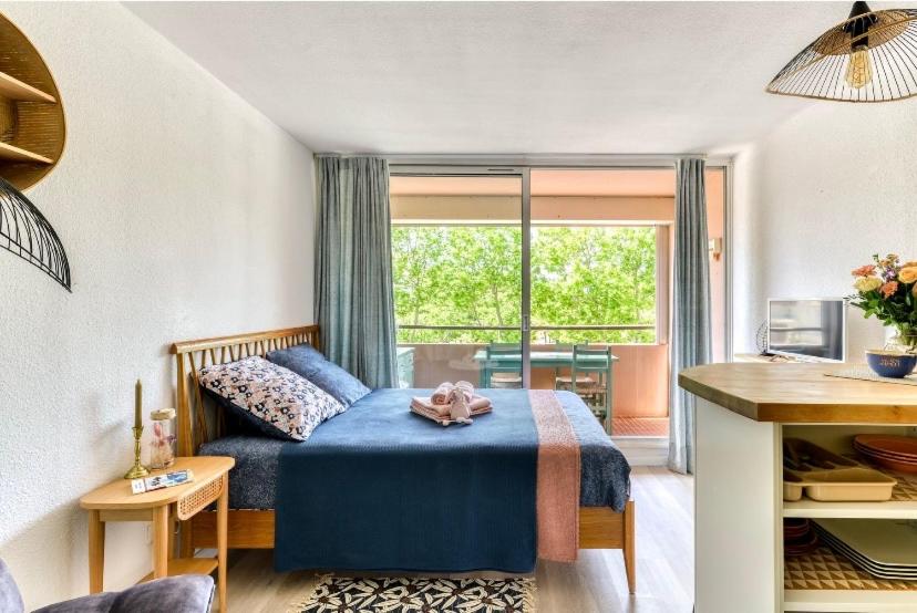a bedroom with a blue bed and a large window at Studio Les Régates avec loggia et parking gratuit Plage du Grazel Gruissan in Gruissan