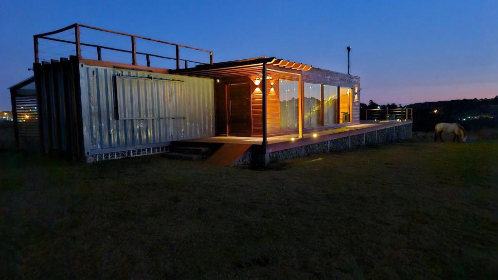 ein kleines Haus auf einem Feld mit einem Pferd im Hintergrund in der Unterkunft Refúgio Serra Lebre: Cabana Luxo Panorâmica em 6 Hectares de Araucárias in São Francisco de Paula