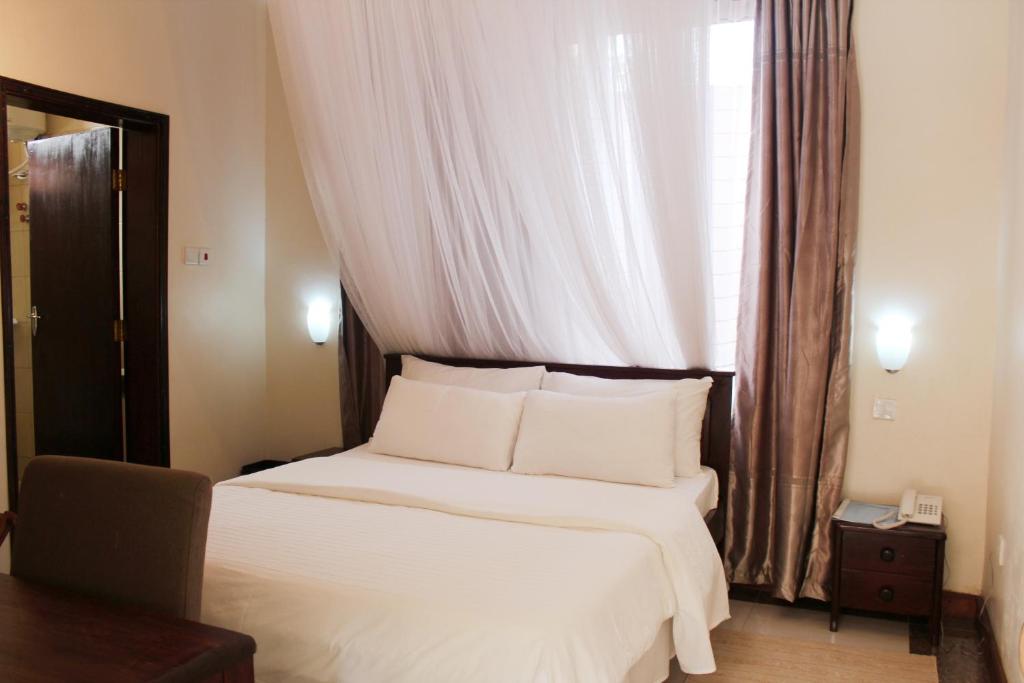 um quarto com uma cama com lençóis brancos e uma janela em Al-Nisaa Hotel and Spa em Jinja