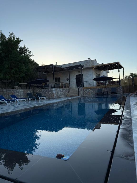 a swimming pool with chairs and a building in the background at Oak Farm مزرعة البلوط in Ajloun