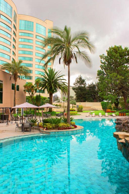 a large swimming pool with palm trees and buildings at K Suites in Quito
