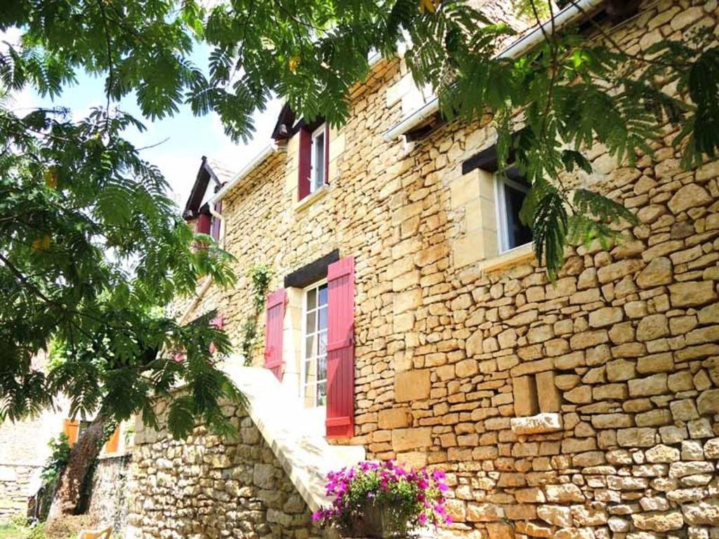 - un bâtiment en pierre avec une porte rouge et des fenêtres dans l'établissement Maison Périgourdine avec jardin, à 5 km de Sarlat, 2 chambres, équipements bébé, animaux acceptés - FR-1-616-58, à Saint-Vincent-le-Paluel