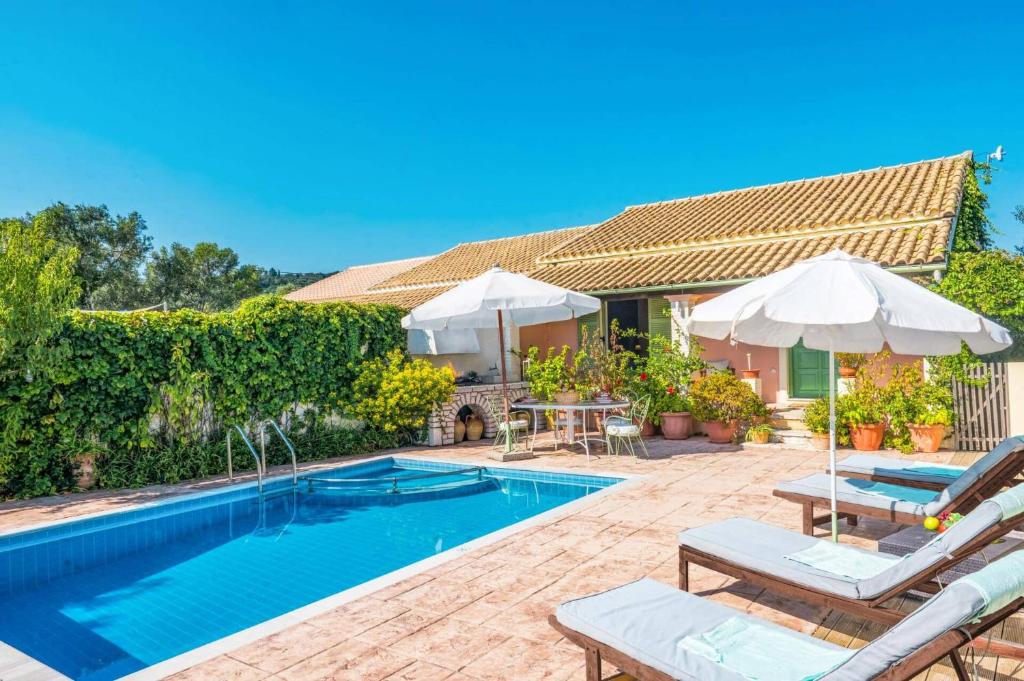 a swimming pool with chairs and umbrellas next to a house at Villa Maistro Cottage by Villa Plus in Ágios Stéfanos