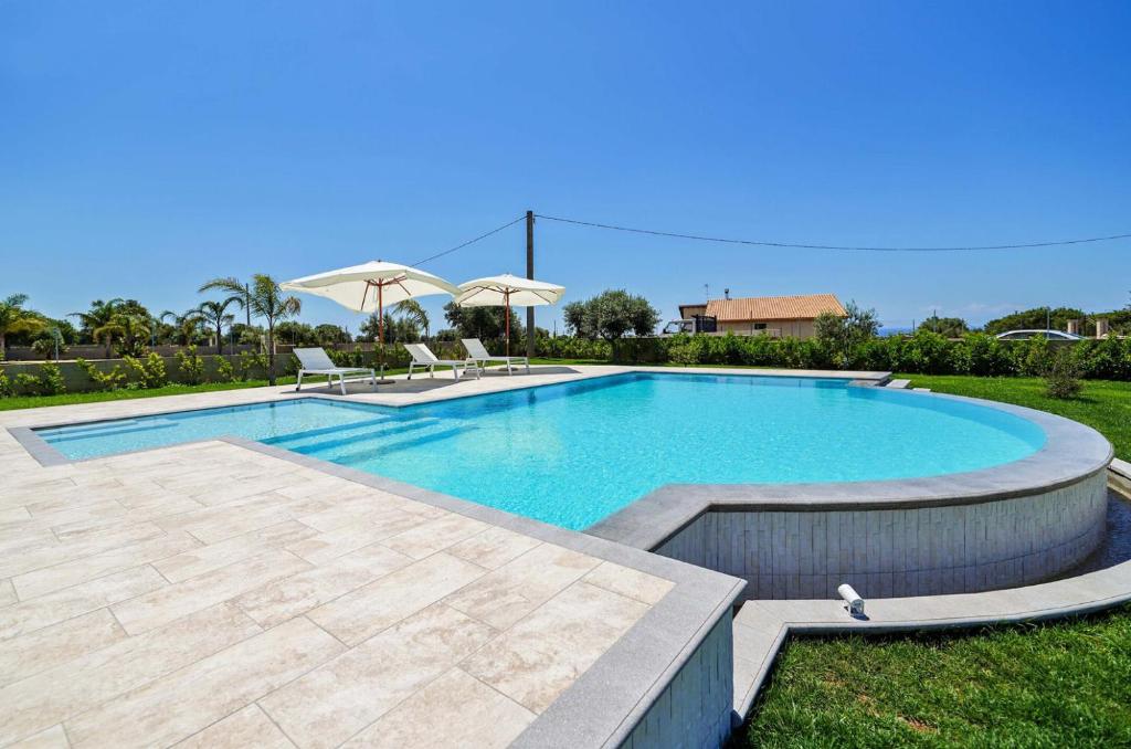 a swimming pool in a yard with chairs and umbrellas at Villetta Bianca in Scicli