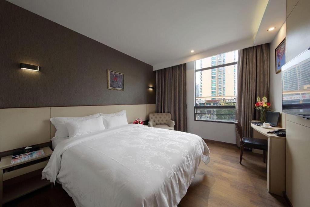 ein Hotelzimmer mit einem großen weißen Bett und einem Schreibtisch in der Unterkunft Hanyong Hotel Shenzhen International Exhibition Center in Fenghuangwei