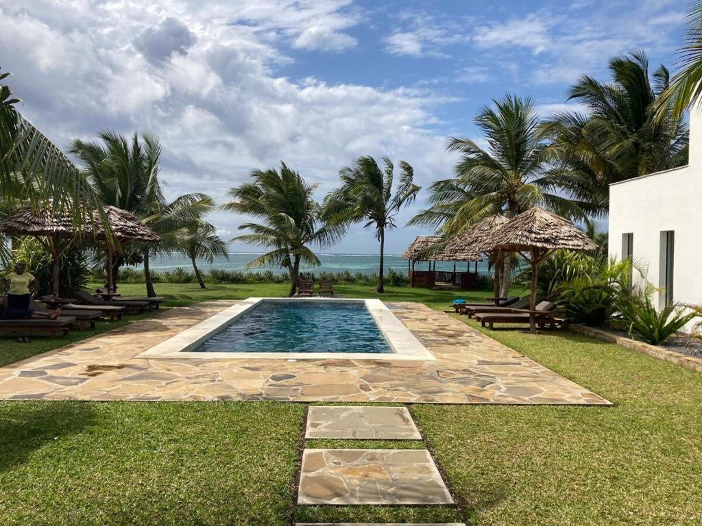 a swimming pool in the middle of a yard with palm trees at Ahadi Beachfront by YourHost 2 bedroom Kilifi in Mombasa