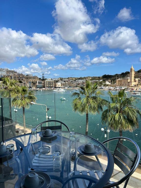 a table with a view of a harbor with palm trees at Bay Seafront Apartment in Marsaskala