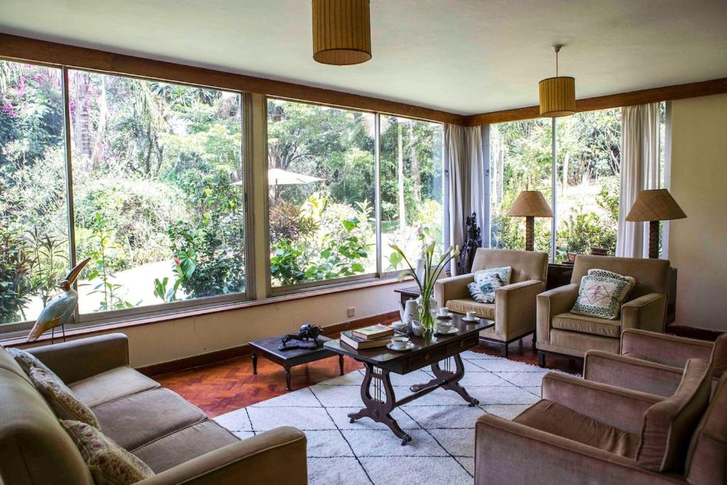 a living room with couches and a table and large windows at Beautiful Historic House by YourHost Nairobi in Nairobi