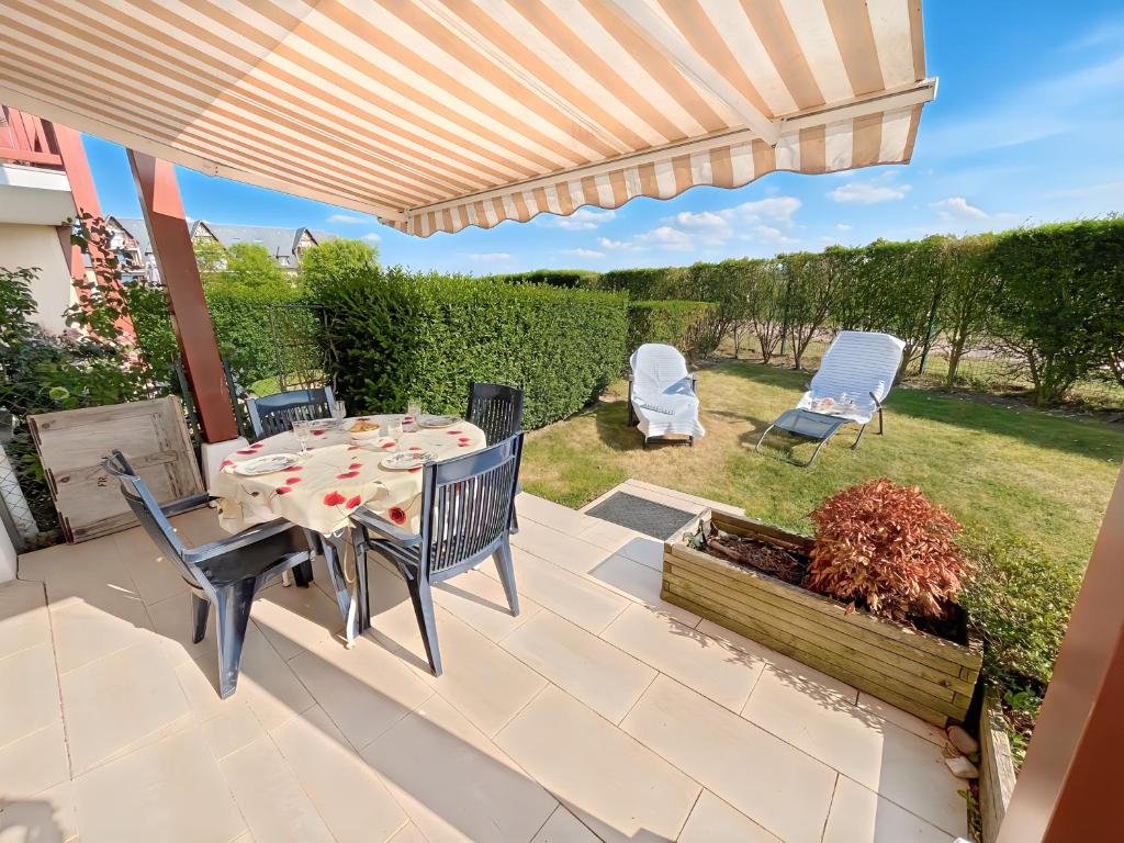 un patio avec une table et des chaises sous une pergola dans l'établissement Le Jardin de Blonville - À 10 min à pied de la plage - tennis & équitation à côté, à Blonville-sur-Mer