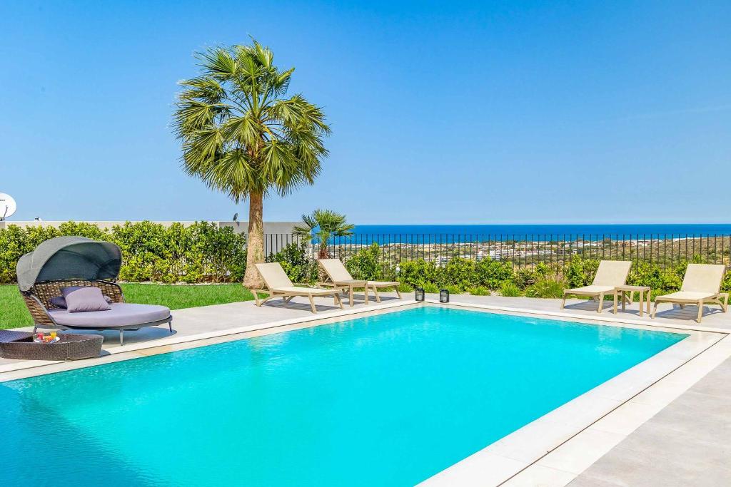 una piscina con sillas, una palmera y el océano en Kamelia Villa 3, en Hersonissos