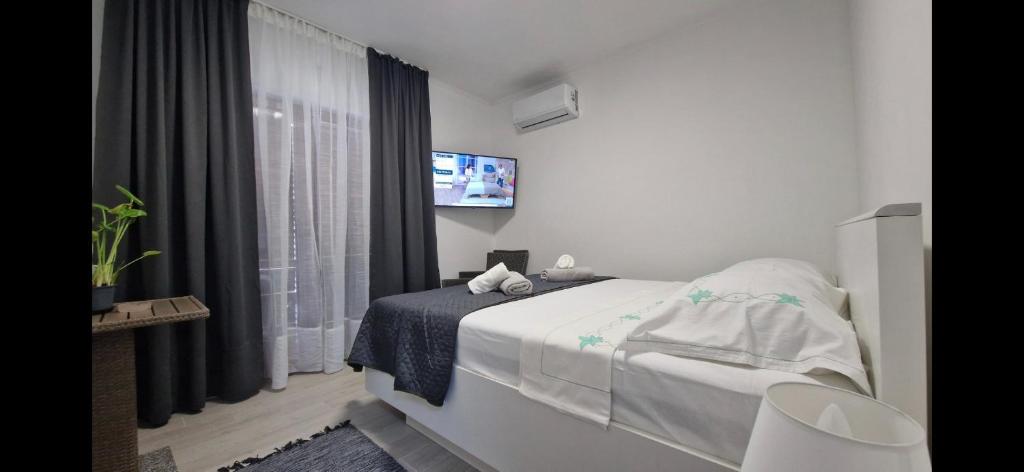 a white bedroom with a bed and a tv at Apartmani Deniza 2 guests in Brodarica