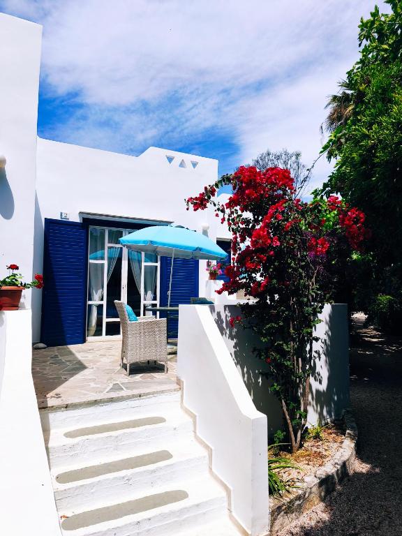 a white house with a blue umbrella and red flowers at Bungalows Ingrid in Tolo