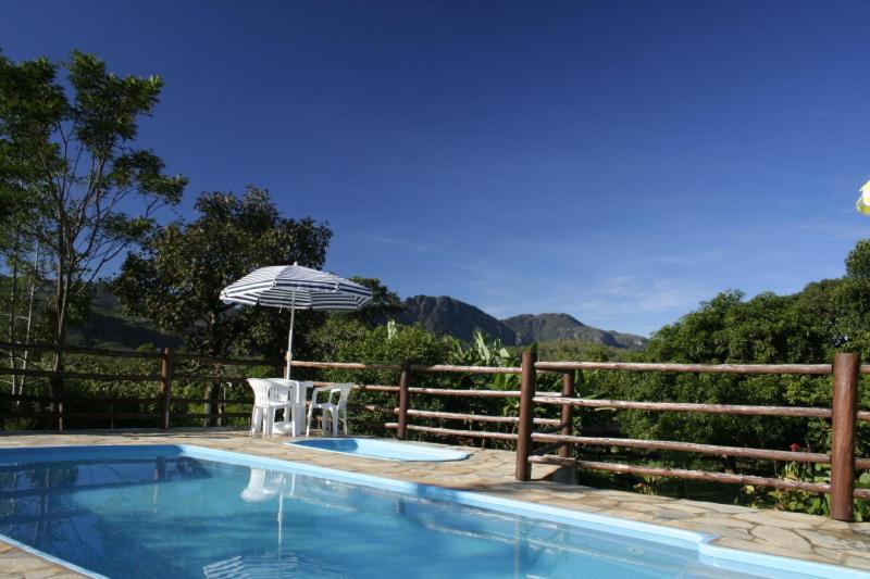 a swimming pool with a chair and an umbrella at Pousada Vale das Araras in Cavalcante