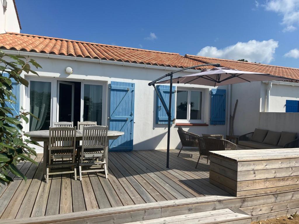 une terrasse en bois avec une table, des chaises et un parasol dans l'établissement Charmante Maison de Plage, à Bretignolles-sur-Mer