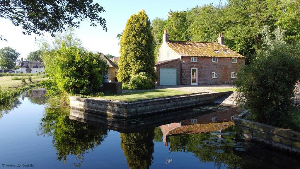 una casa accanto a un fiume con il suo riflesso nell'acqua di Wherry Cottage in Irstead on the Norfolk Broads a Neatishead