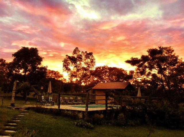 um pôr-do-sol sobre uma piscina com uma casa e árvores em Pousada Vale das Araras em Cavalcante