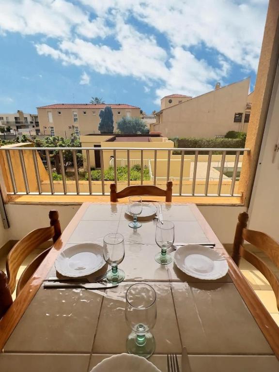 une table avec des assiettes et des verres sur un balcon dans l'établissement Agréable appartement avec piscine, à Valras-Plage