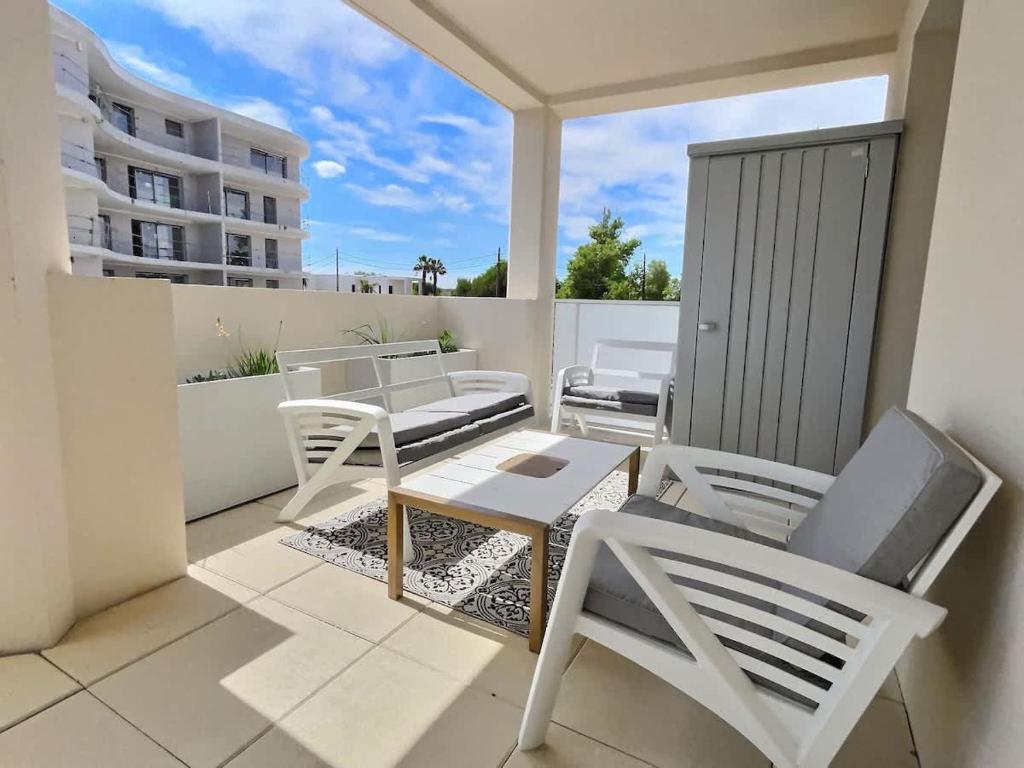 d'un balcon avec des tables et des chaises blanches. dans l'établissement Appartement spacieux et lumineux dans une résidence à 650m de la mer, à Sérignan