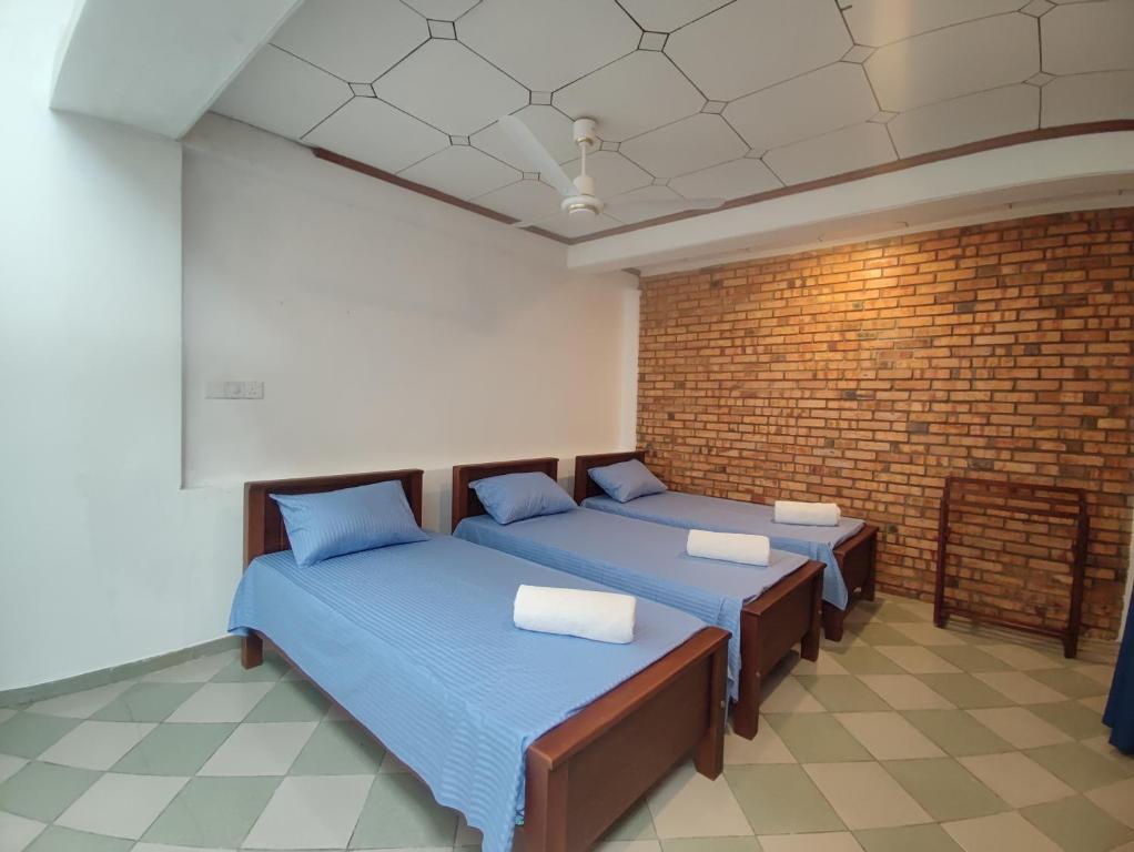 ein Zimmer mit zwei Betten und einer Ziegelwand in der Unterkunft Chandra Holiday Home in Dikwella