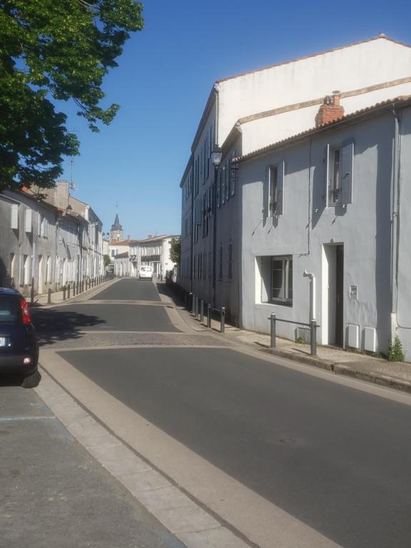 an empty street with white buildings and a car at La Maison Blanche in Dompierre-sur-Mer