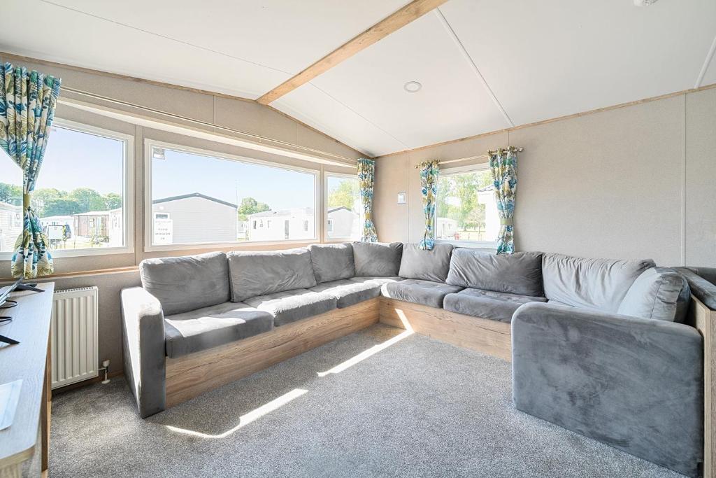 a living room with a large couch and windows at Dune Delight - Hayling Island in South Hayling