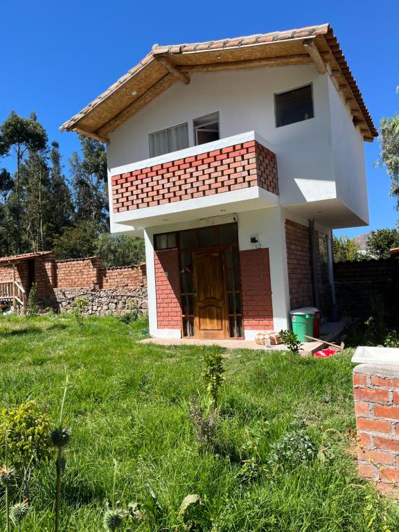 une petite maison avec une pelouse verte en face de celle-ci dans l'établissement Casa de Marguito, à Urubamba