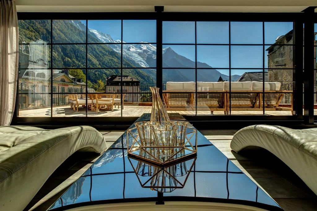 une chambre avec une table en verre devant une grande fenêtre dans l'établissement Penthouse Le Lustre, à Chamonix-Mont-Blanc