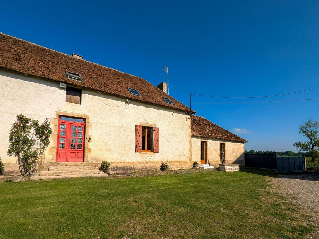 a building with a red door and a grass yard at Gîte à la ferme avec jardin privé, clim et visite de l'exploitation près d'Argenton-sur-Creuse - FR-1-591-321 in Cluis