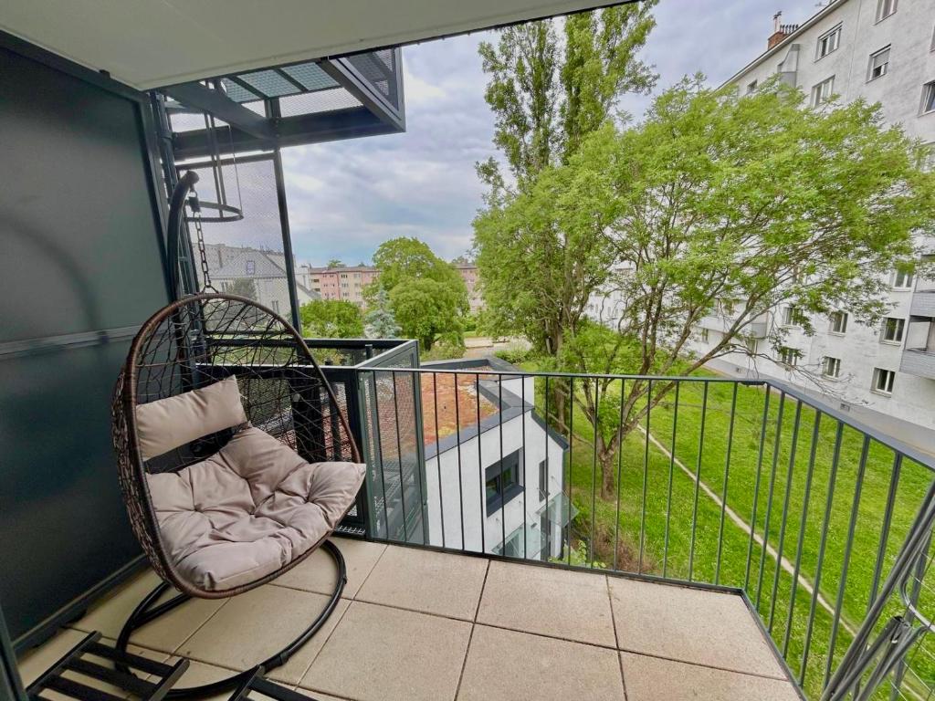 ein Balkon mit Rattanstuhl und Blick auf einen Park in der Unterkunft Modern Danube Apartment with Balcony & Free Parking in Wien