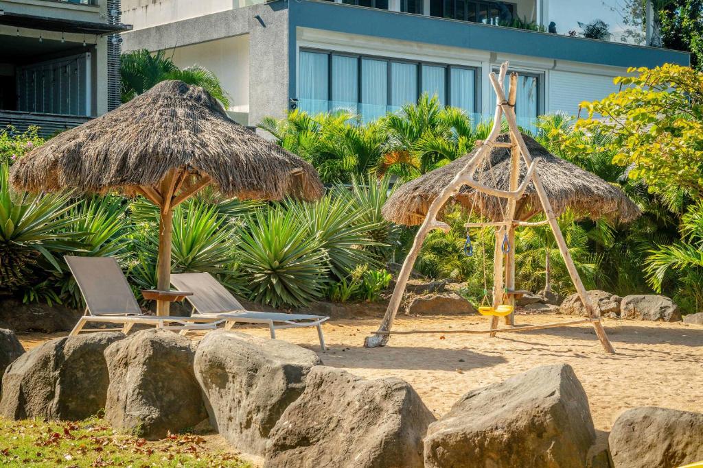 two straw umbrellas and chairs on a beach at Soma Bay - Incredible Seaside Apartment in Tamarin