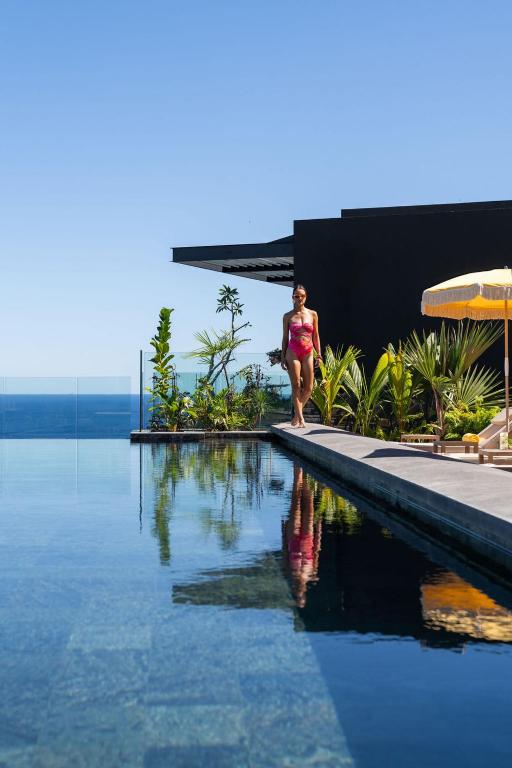 a woman in a bikini walking next to a swimming pool at Legend Hill Residences and Spa in Rivière Noire