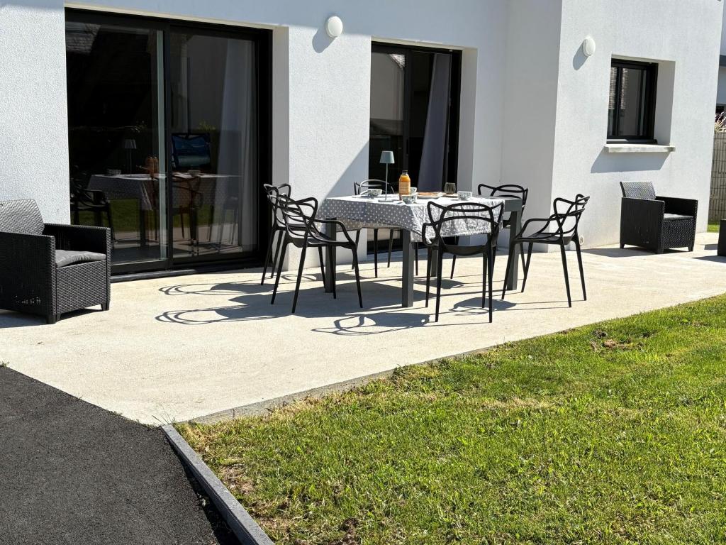 a dining table and chairs on a patio with grass at La Villa Bianca - A 10 min à pied de la plage in Bénodet