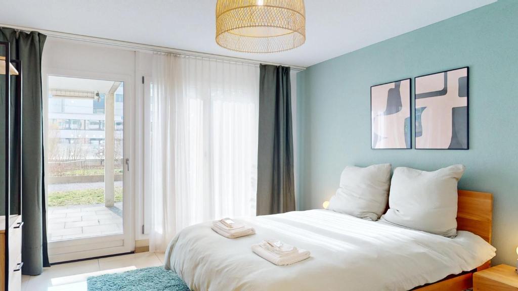 a bedroom with a white bed with a large window at Gartenwohnung, nahe Zentrum Zürich und Flughafen in Wallisellen