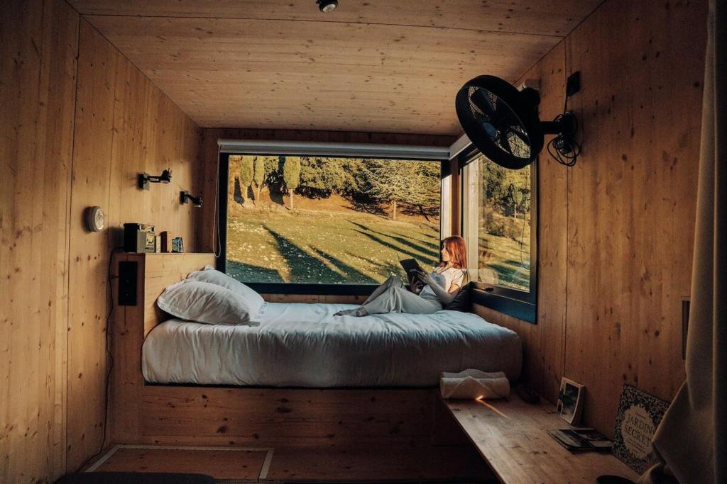 una donna seduta su un letto in una stanza con finestra di Parcel Tiny House Barroux, entouré par les lamas près du Mont Ventoux a Le Barroux