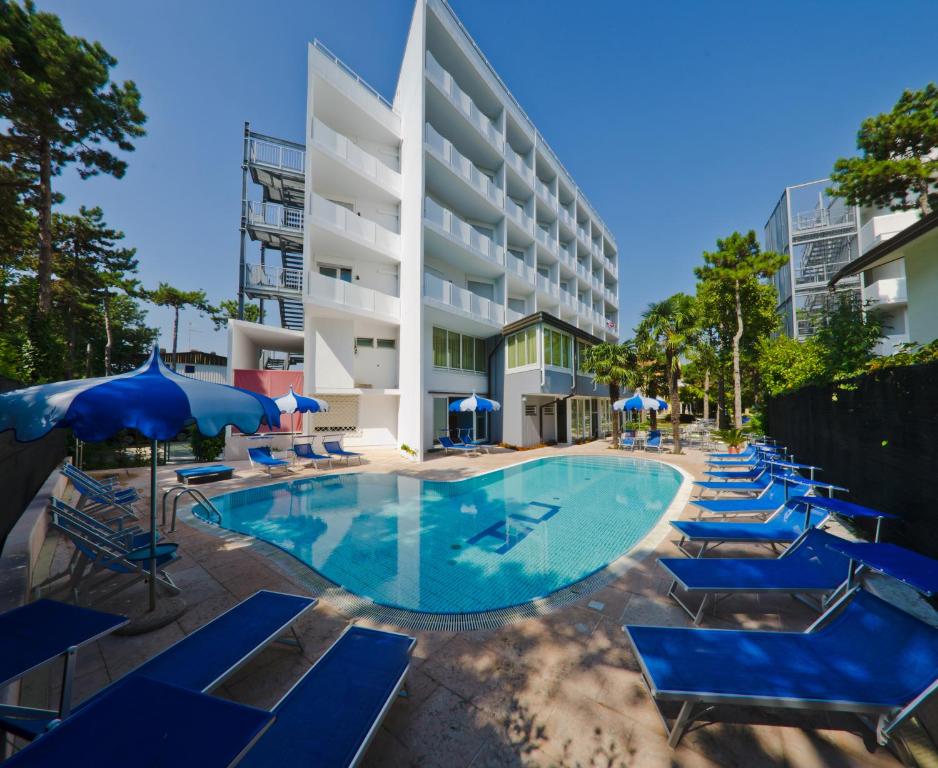 a pool with blue chairs and umbrellas in front of a building at Hotel Carlton in Lignano Sabbiadoro