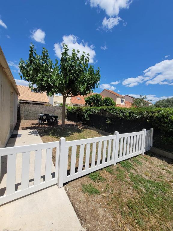 une clôture blanche dans une cour avec un arbre dans l'établissement Petite maison avec jardin à 10min des plages, à Villeneuve-lès-Maguelone